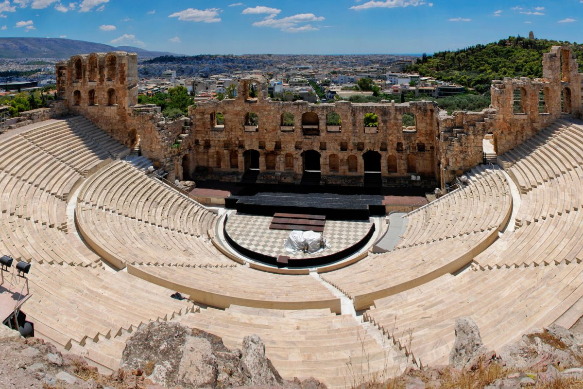 The Odeon of Herodes Atticus in Athens, Greece, an ancient stone theater with semicircular seating and a stage, set against the cityscape.